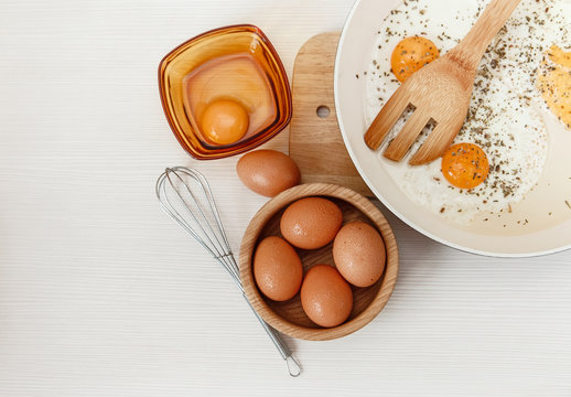 Fried eggs in the frying pan,breakfast ingredients,kitchen accessories.Fresh Brown Eggs in the Wooden Plate.Cooking morning food.White Background.Top View.Food background