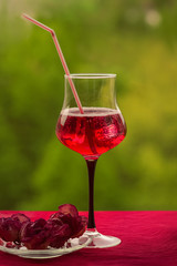 one glass with red drink on a red table , on green background