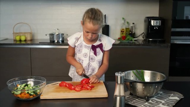 Little girl preparing salad in the kitchen - has cut her finger while slicing tomatoes