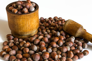 Heap of hazelnuts in a wooden mortar with a wooden pestle on a white background