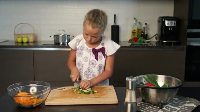 Little girl slicing cucumbers for the salad in the kitchen