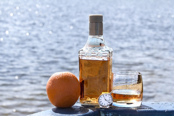 Bottle tequila and tumbler with watches on shore of lake