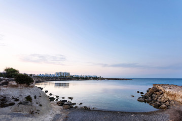 Photo of sea in protaras, cyprus island, with rocks and hotels at sunset.