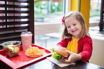 Little girl eating a hamburger in fast food restaurant