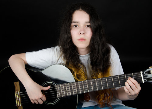 Teenage girl with painted hair playing a black guitar (on a black background)