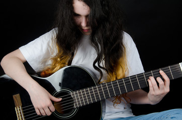 Teenage girl with painted hair playing a black guitar (on a black background)