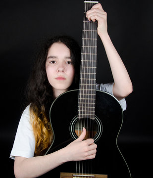 Teenage girl with painted hair holding a black guitar (on a black background), selective focus on the guitar and hands