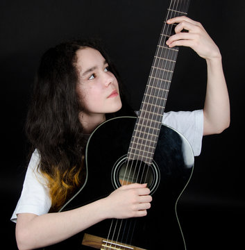 Thoughtful teenage girl playing a black guitar (on a black background)
