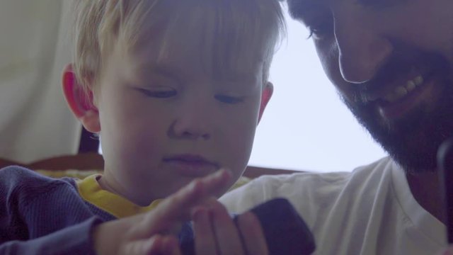 Uncle looks over the shoulder of his nephew as he plays games on a cell phone 