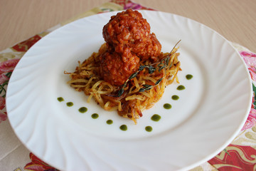 Meatballs in sweet and sour tomato sauce on a crispy crust of potatoes