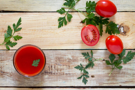 Glass of tomato juice with green leaves on a wooden background,