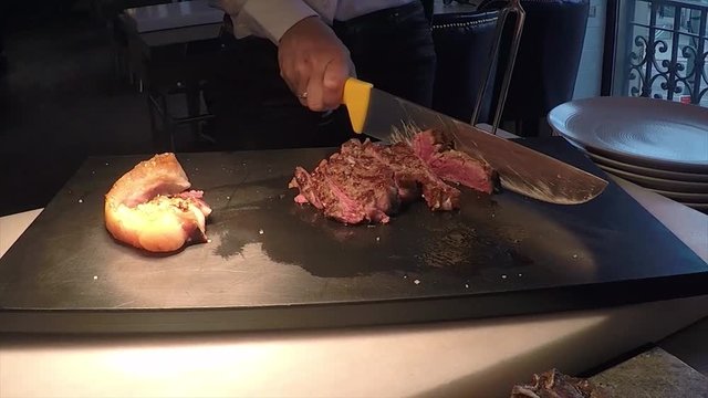 Professional beaf steak meat cut servise with special equipment and women's hands on a black kitchen board before eating