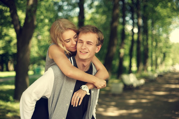 Happy young couple. Beautiful smiling blonde girl hugging her boyfriend from the back.