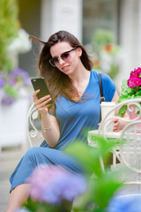 Portrait of young beautiful woman sitting in outdoor cafe drinking coffee and using smartphone.