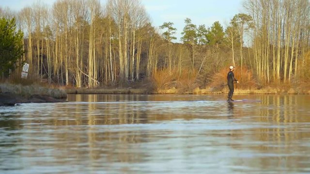 Man in wetsuit glides on river water while on SUP board