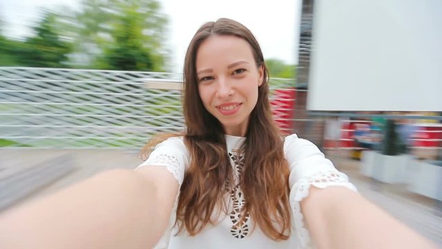 Young girl making video selfie and having fun in the park. Lifestyle selfie portrait of young positive woman having fun and taking selfie. Concept fun with new trends and technology.