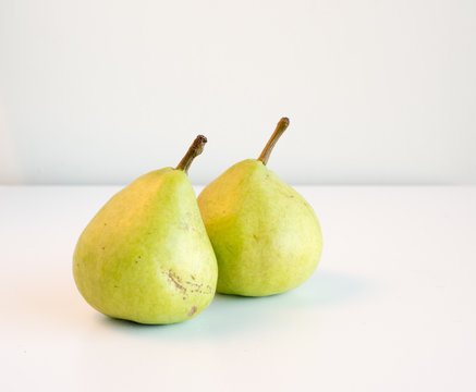 High angle view of two natural looking green pears on a white table