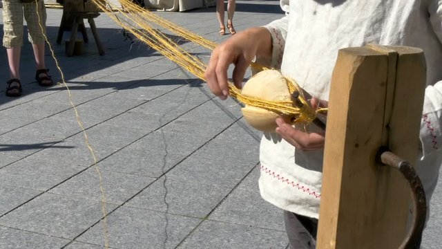 A man holding a ball with strings he seems to make a ball out of the strings in the streetside of the city