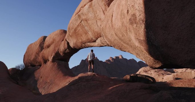 4K male tourist entering into the famous arch of the Spitzkoppe mountains and taking a picture