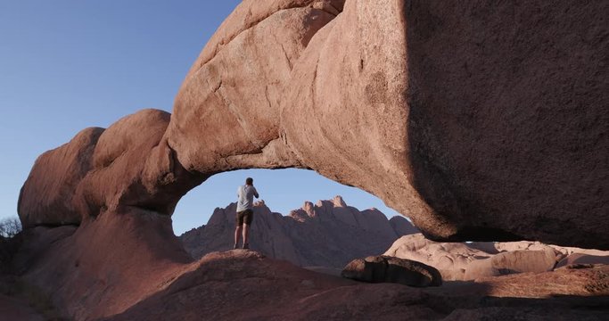 4K male tourist entering into the famous arch of the Spitzkoppe mountains and taking a picture