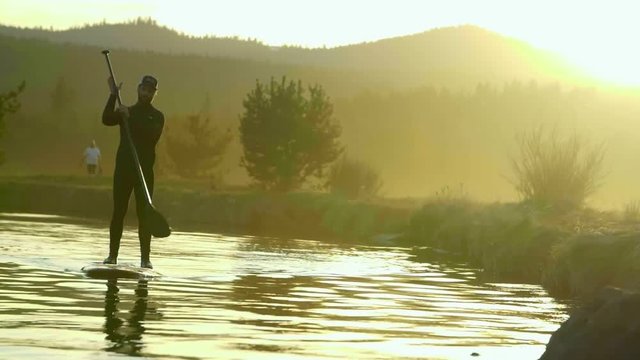 Man in wetsuit paddleboards with a beautiful sunset behind him on Deschutes River in Bend, Oregon
