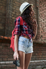 The girl tourist with hat and sunglasses, holding the camera in the background of the red brick building