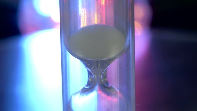 Almost used up sand of the hourglass with the colorful background at the back