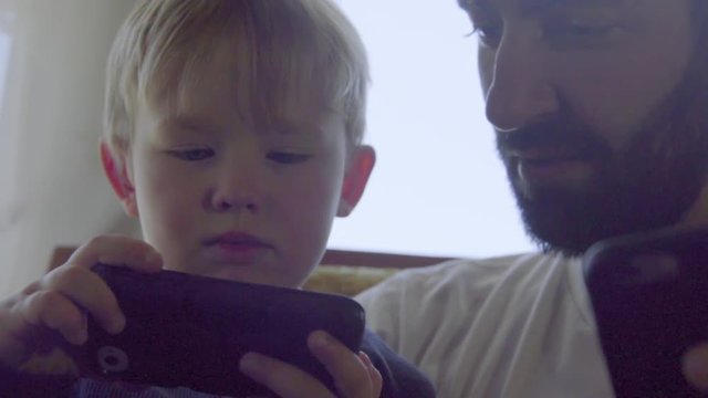 Close up shot of boy and uncle playing on cell phones 