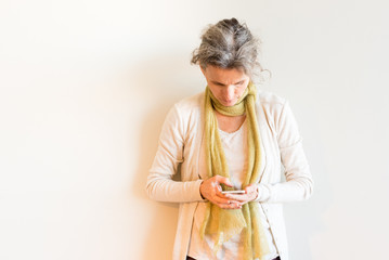 Natural looking middle aged woman with grey hair looking down at smart phone against neutral background © Natalie Board