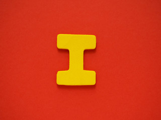 Capital letter I. Yellow letter I from wood on red background. Alphabet vowel.
