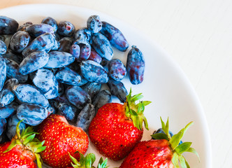 Ripe red strawberry and blue honeysuckle berries on the white pl