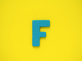 Capital letter F. Blue letter F from wood on Yellow background.