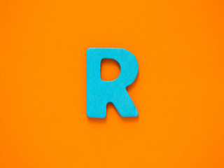 Capital letter R. Blue letter R from wood on orange background.