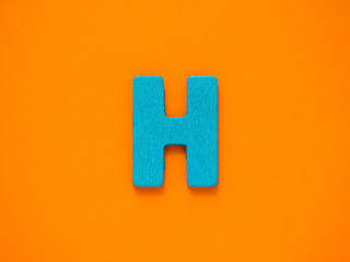 Capital letter H. Blue letter H from wood on orange background.