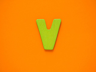 Capital letter V. Green letter V from wood on orange background.