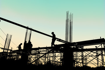 Silhouette of construction workers working on scaffolding at a h - obrazy, fototapety, plakaty