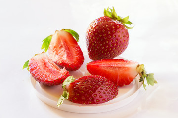Sweet ripe strawberries and a whole and cut into pieces lying on the table in a high key sort of Malvina.