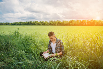 Naklejka na ściany i meble Young man holding book in the green meadow. Free happy man. Knowledge is power. Thirst for knowledge.front sunlight background