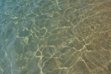 Sun's rays over a transparent water, through which sand is visible.