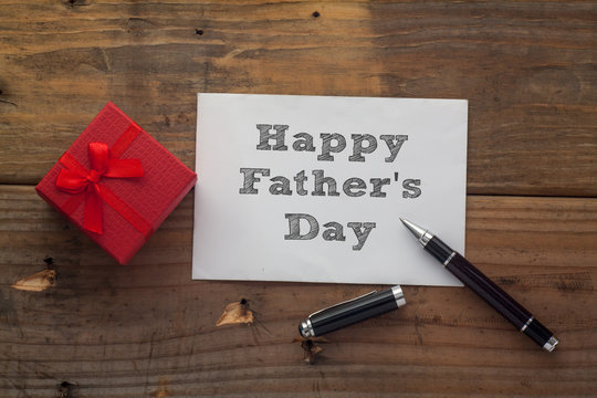 Happy Father's Day written on paper with pen,red gift box and wooden background desk.