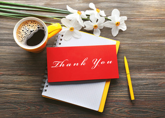 Cup of fresh coffee and greeting card with text Thank You on wooden background