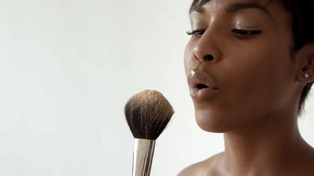 Black attractive woman blows on makeup brush with powder spread in air