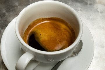 Closeup of coffee in white cup with white saucer and metal spoon