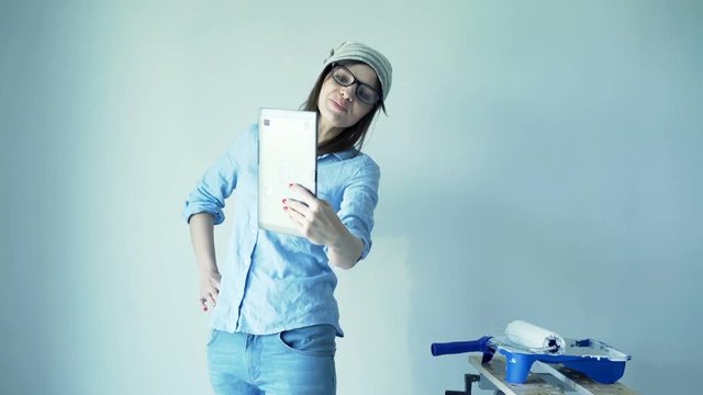 Young woman chatting on tablet during painting ker new home
