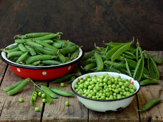 Green pea pods and cleaned in a metal bowl on a wooden background