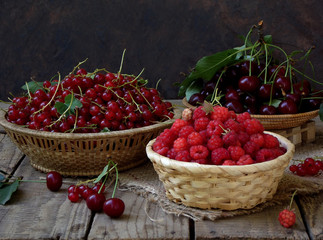 Fresh fruit and berries in baskets on wooden background - red currants, raspberries, cherries