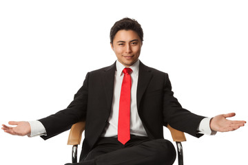 Handsome carefree businessman in a black suit and red tie, leaning back in a chair against a white background looking directly at camera. 