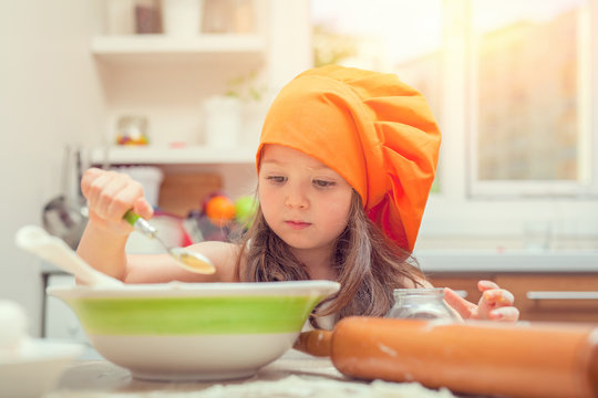 beautiful cute little girl with bonnet making pasta dough in kitchen