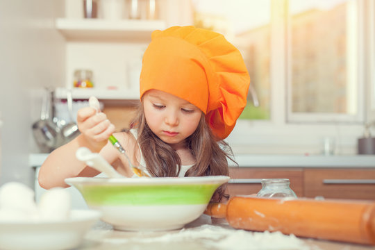 beautiful cute little girl with bonnet making pasta dough in kitchen