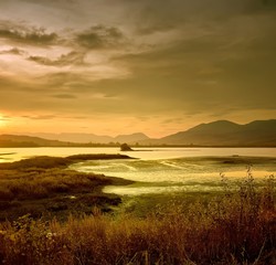 Landscape of foggy sunrise on river shot in natural colors, with grass on foreground and mountains on the horizon. No color correction.